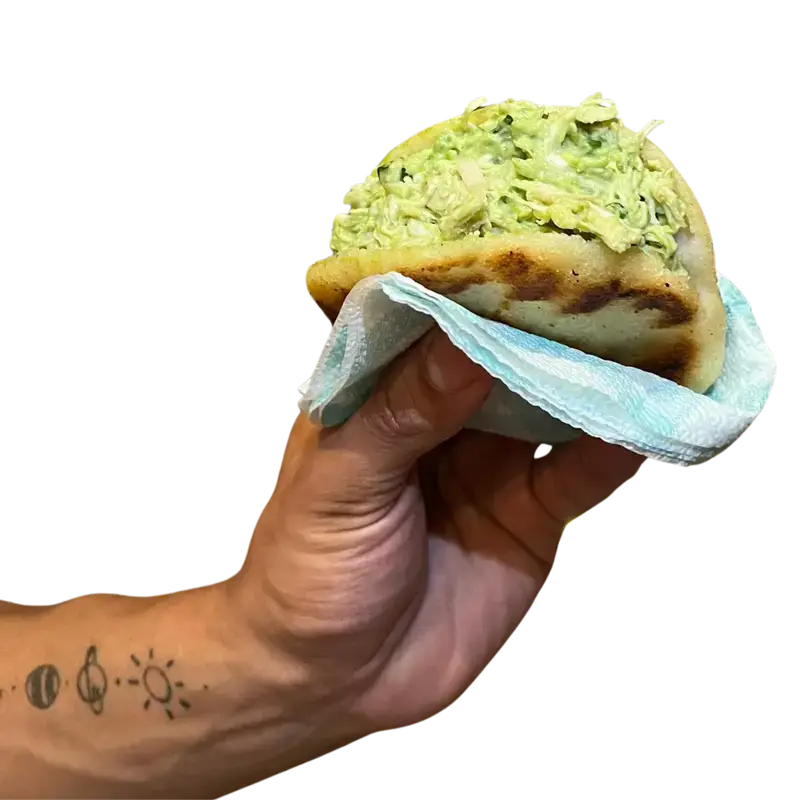Mano con una Arepa La Reina, rellena de pollo, aguacate, cebollin. Una reina pepiada Venezolana.